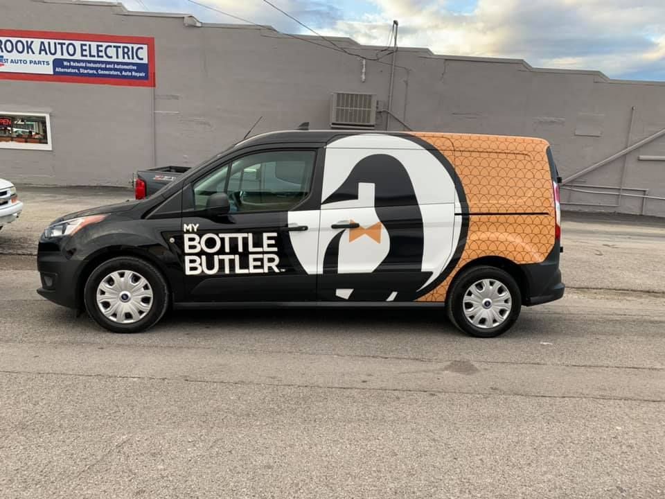 A bottle butler van is parked in front of a building.