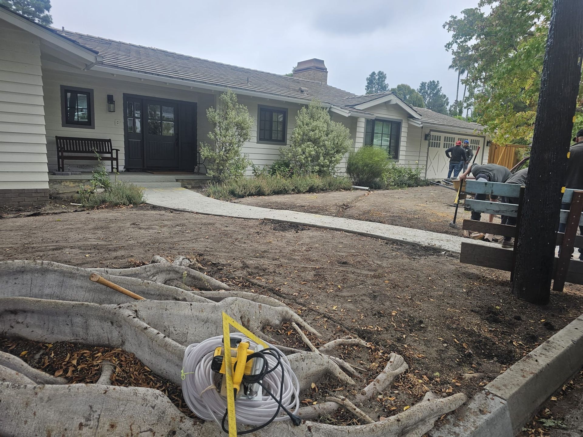 House exterior with yard being worked on; a walkway leads to the front door. Man is working in the yard.