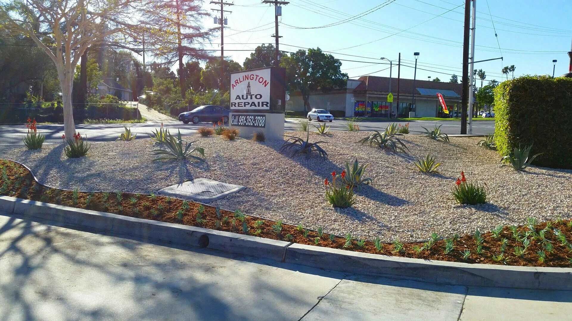 Landscaped island with a sign for a business, featuring a gravel base, succulents, and flower beds.