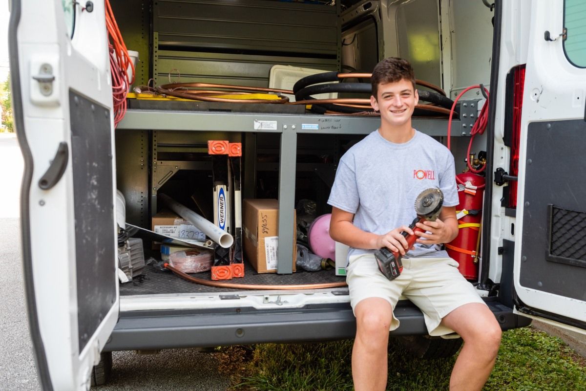 A young man is sitting in the back of a van holding a wrench.