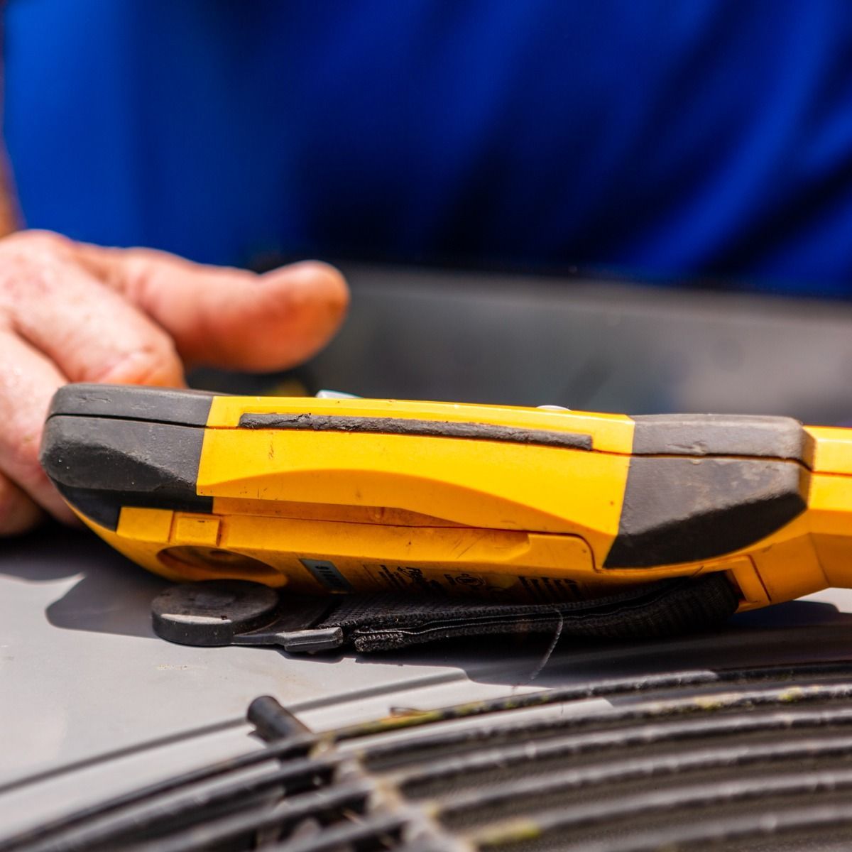 A person is holding a yellow and black device on top of an air conditioner.