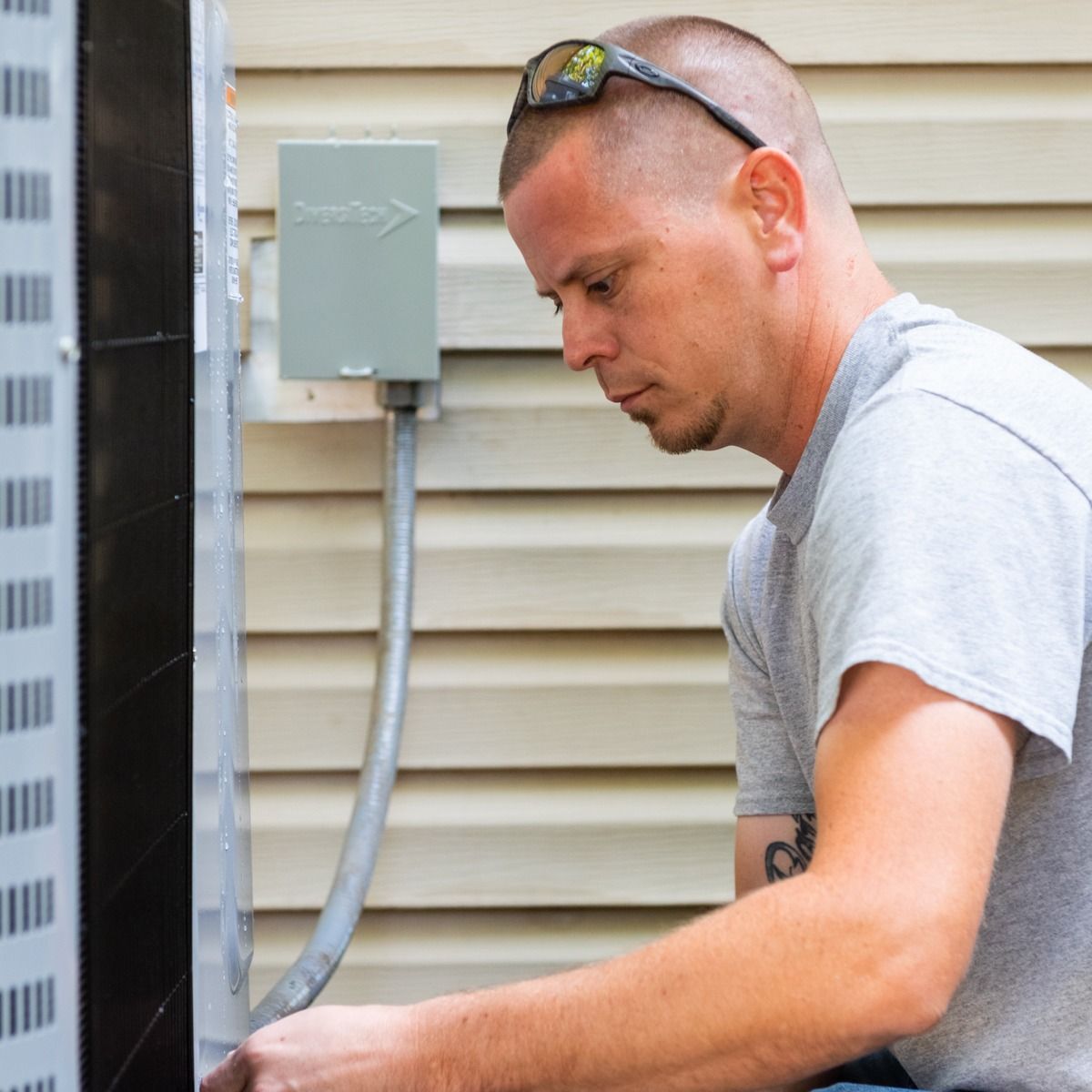 A man is working on an air conditioner outside of a house.