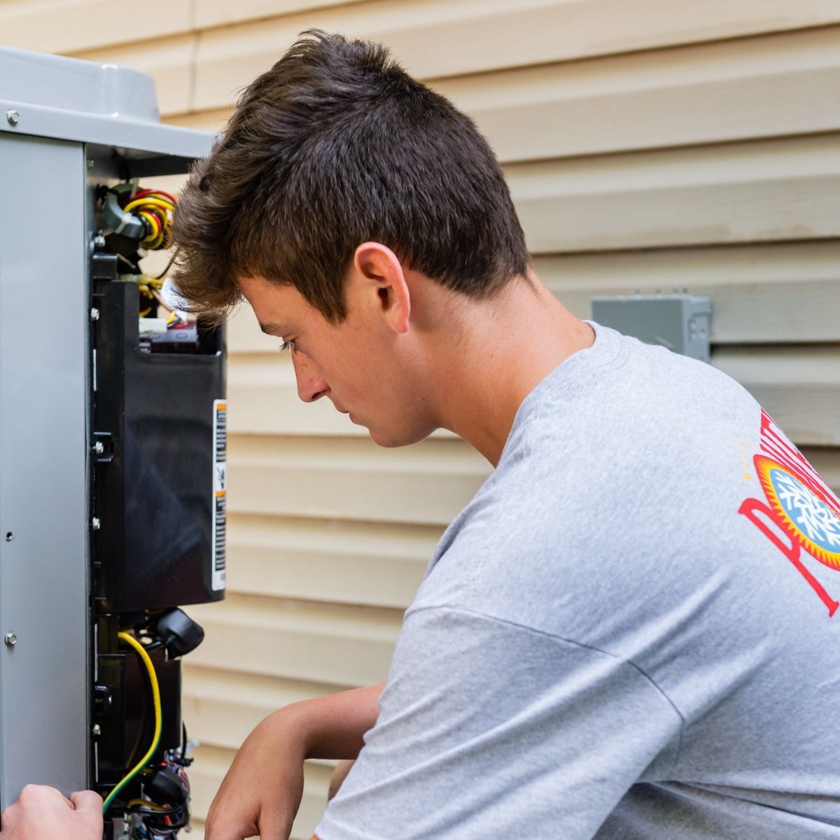 A man wearing a grey shirt with a red r on the back is working on a machine