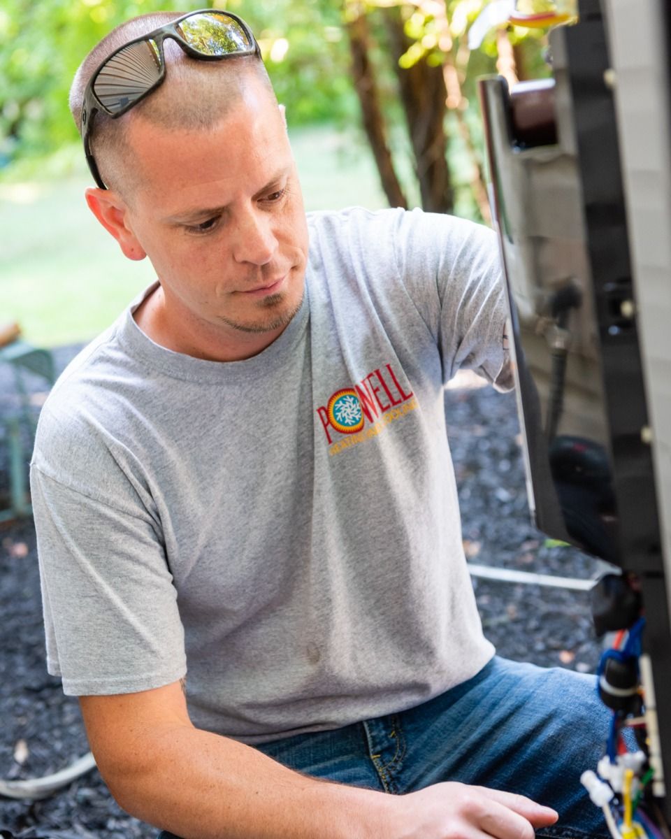 A man wearing sunglasses and a grey shirt with the word rc on it is working on a machine.