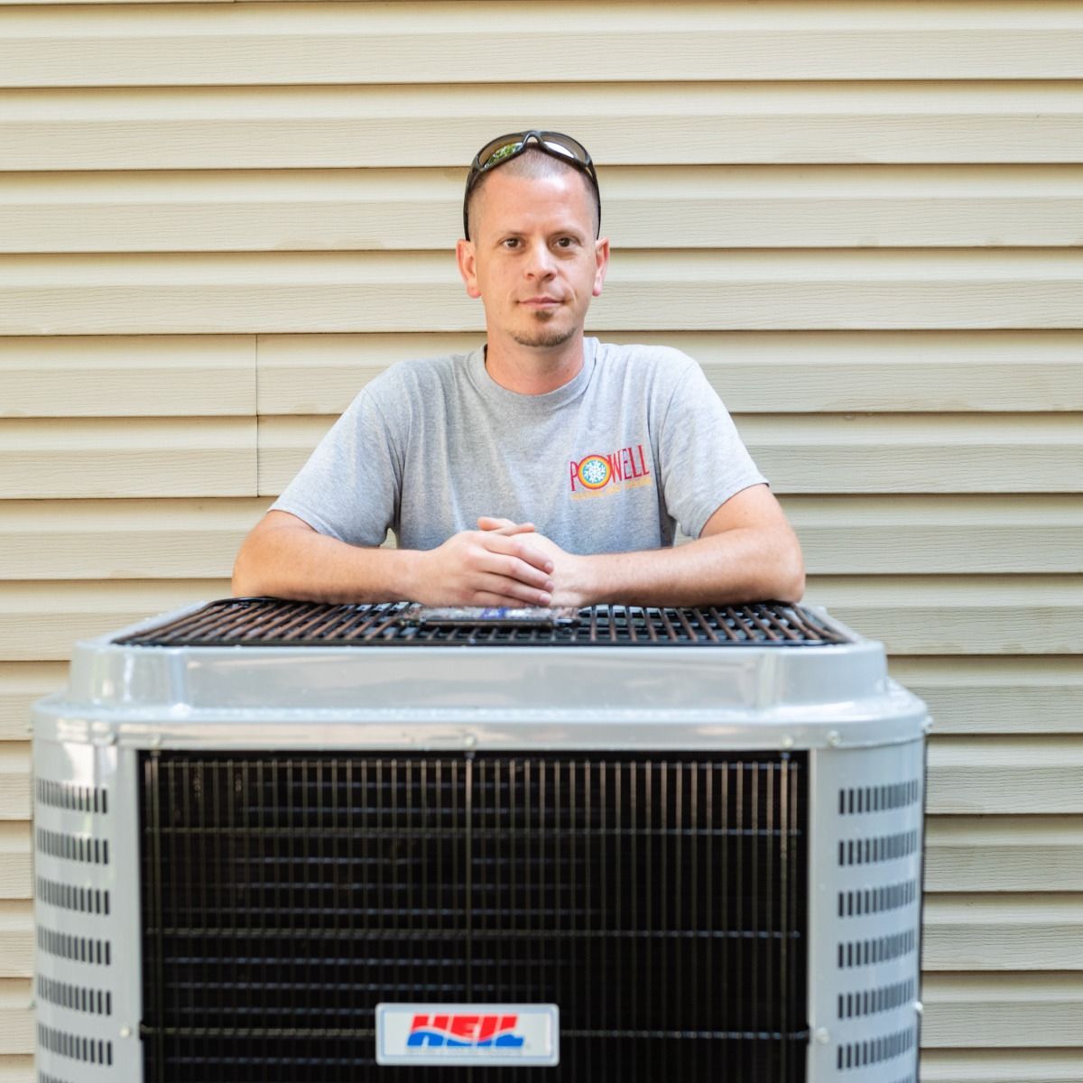 A man in a grey shirt is leaning on an air conditioner