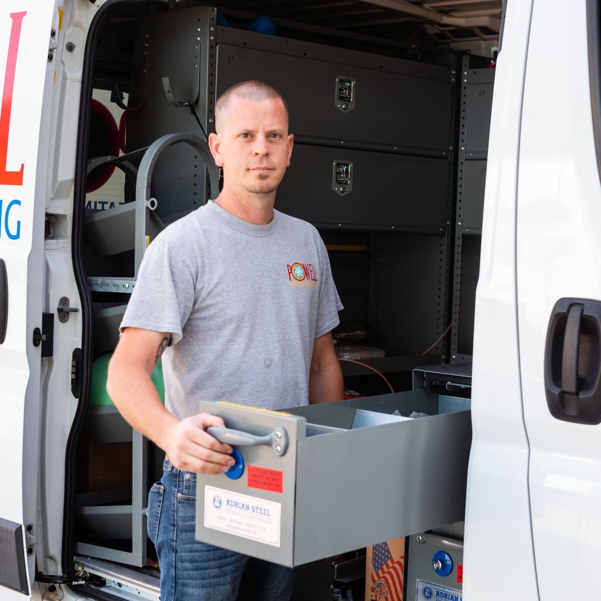 A man is standing in the back of a van holding a toolbox