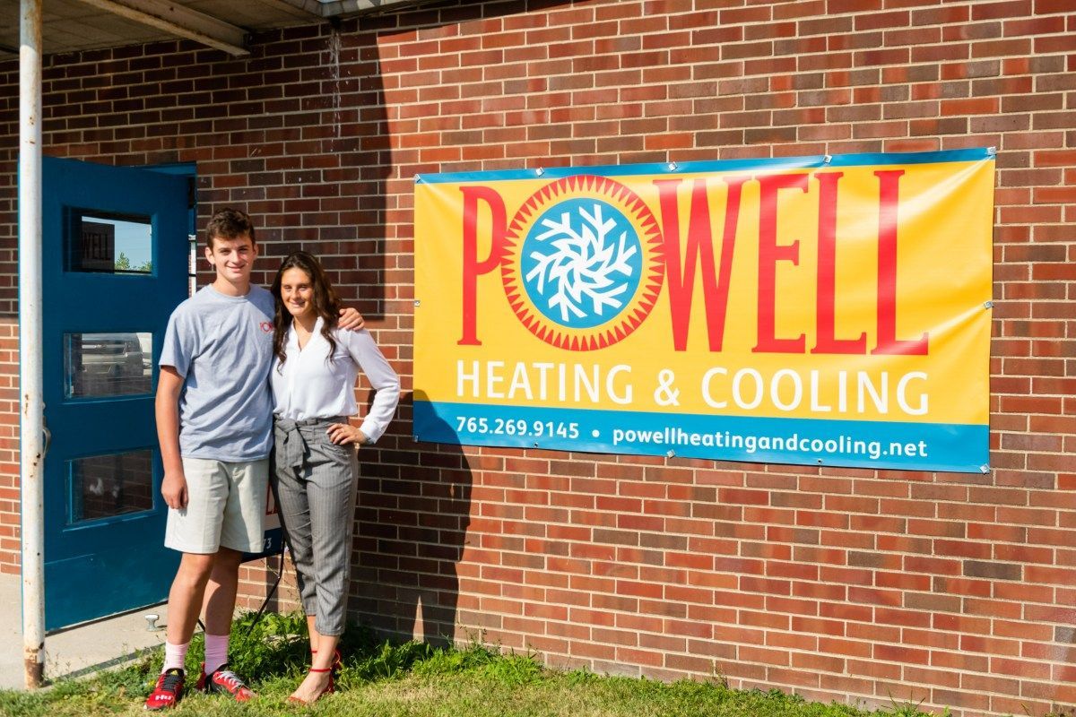 A man and a woman are standing in front of a powell heating and cooling sign.