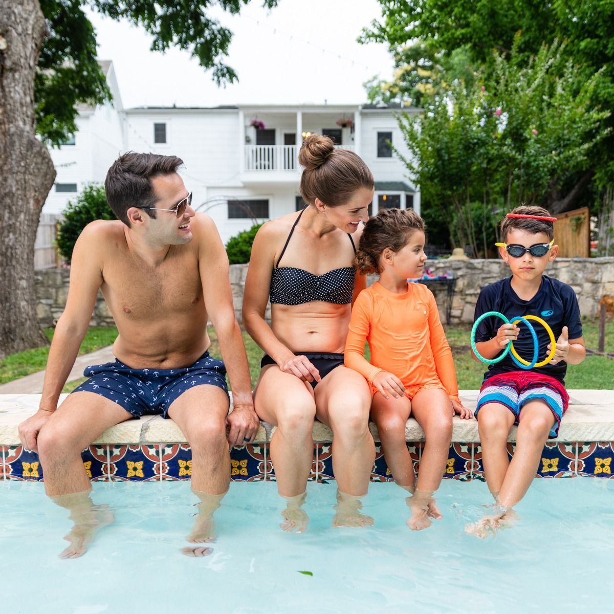 A family is sitting on the edge of a swimming pool.