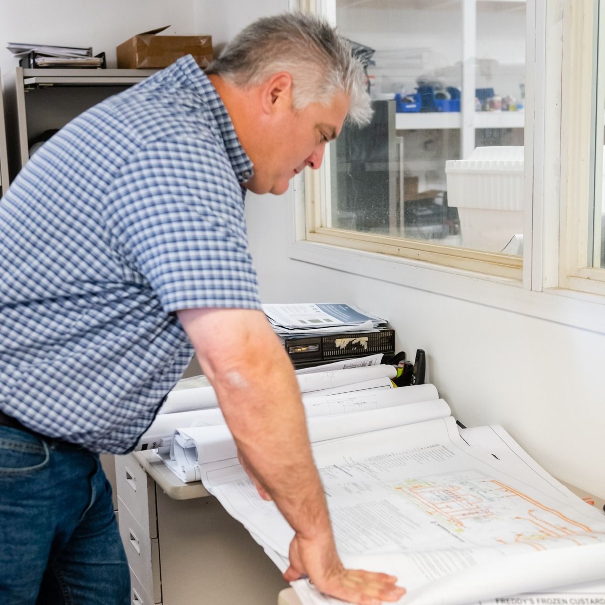 A man in a plaid shirt is looking at a blueprint