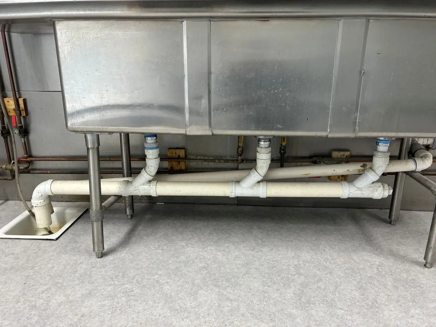 Stainless steel industrial tank with white pipes and valves in a utility room.