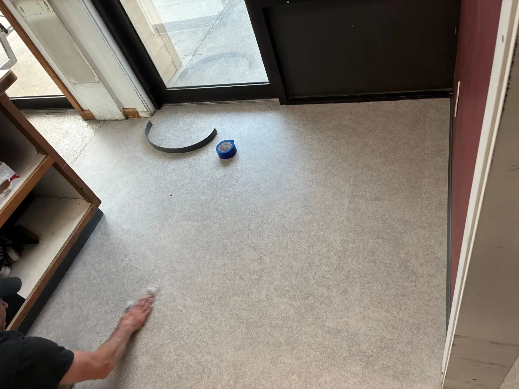 Person reaching toward a small blue object on a beige floor by a sliding glass door.