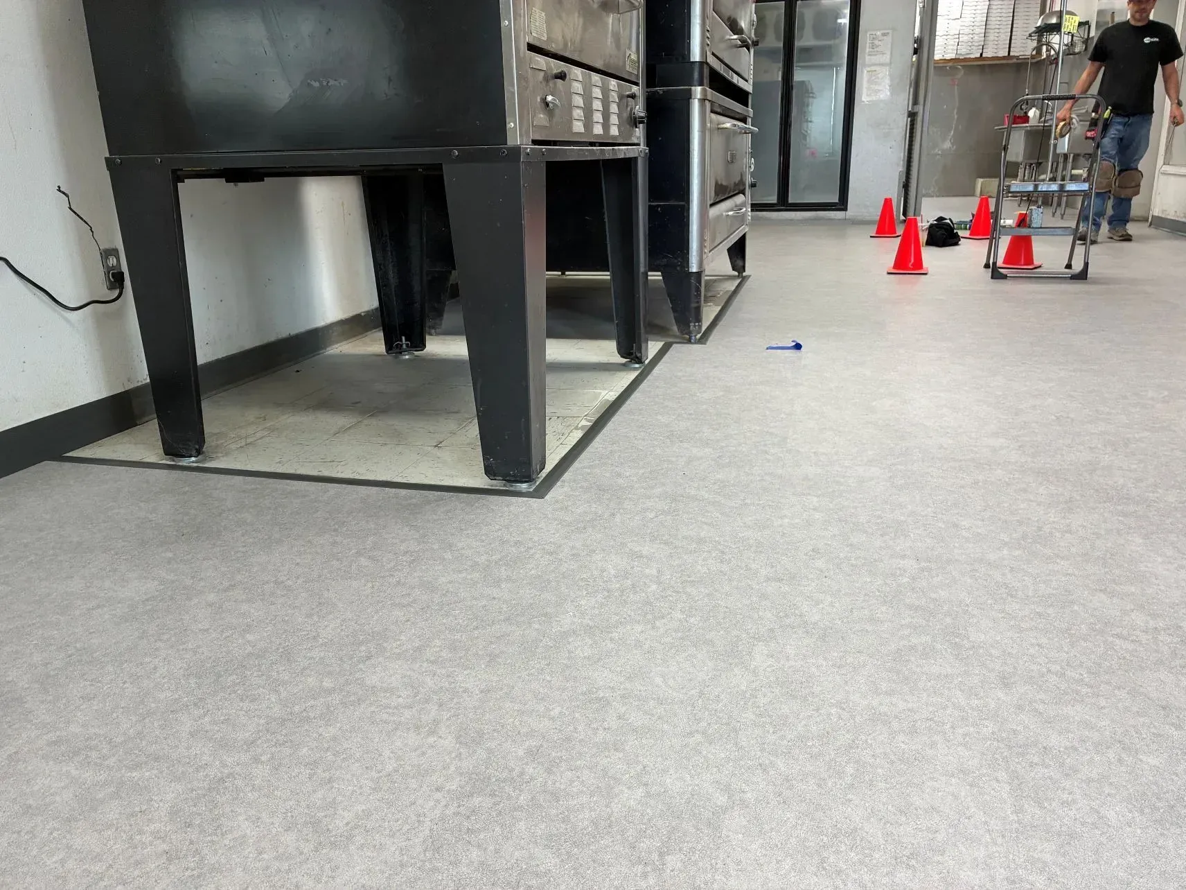 Indoor training area with orange cones, a person pushing a cart, and large black metal equipment.