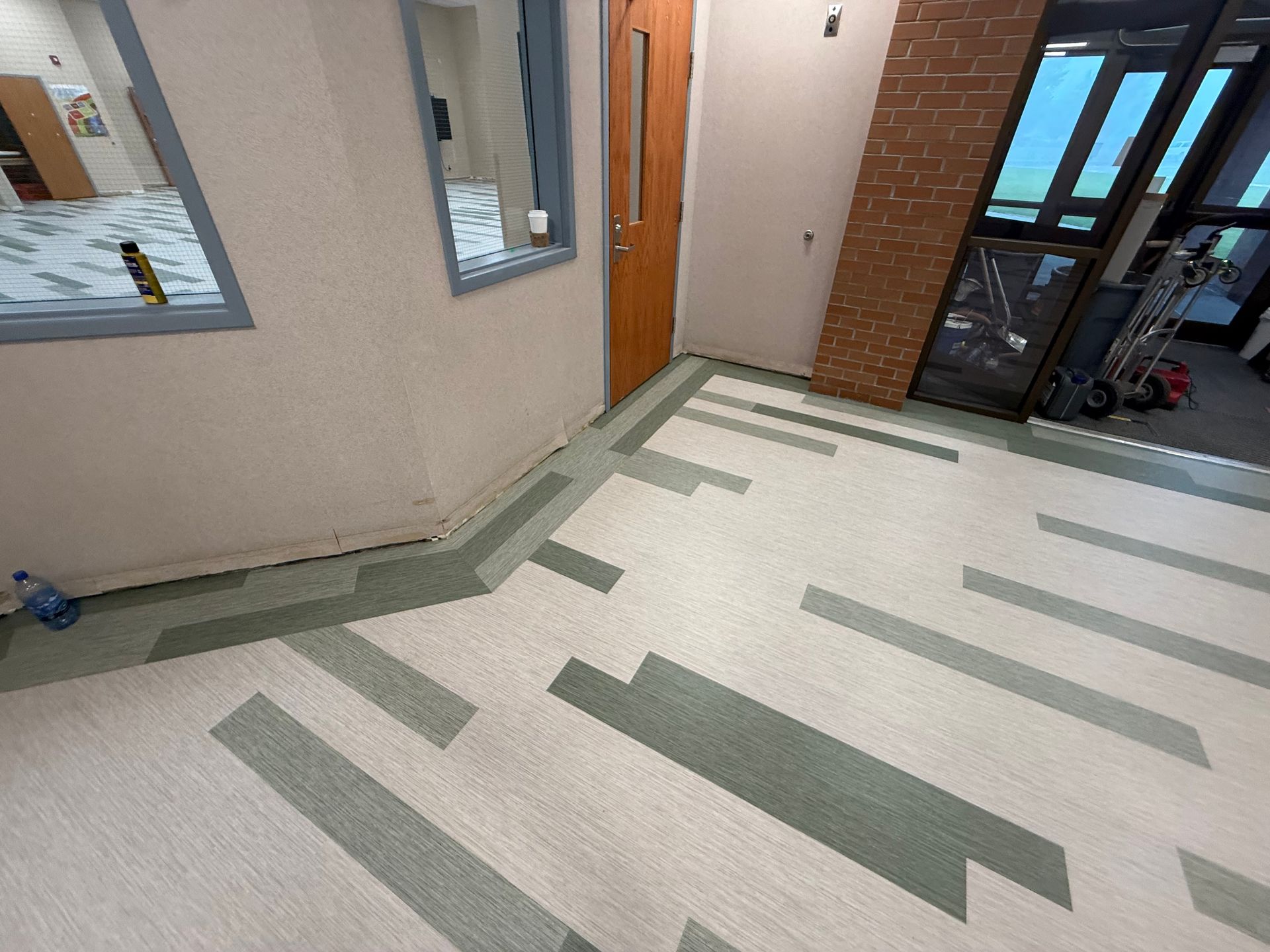 Hallway with light tile floor, beige walls, orange door, windows, and brick wall near an entrance.