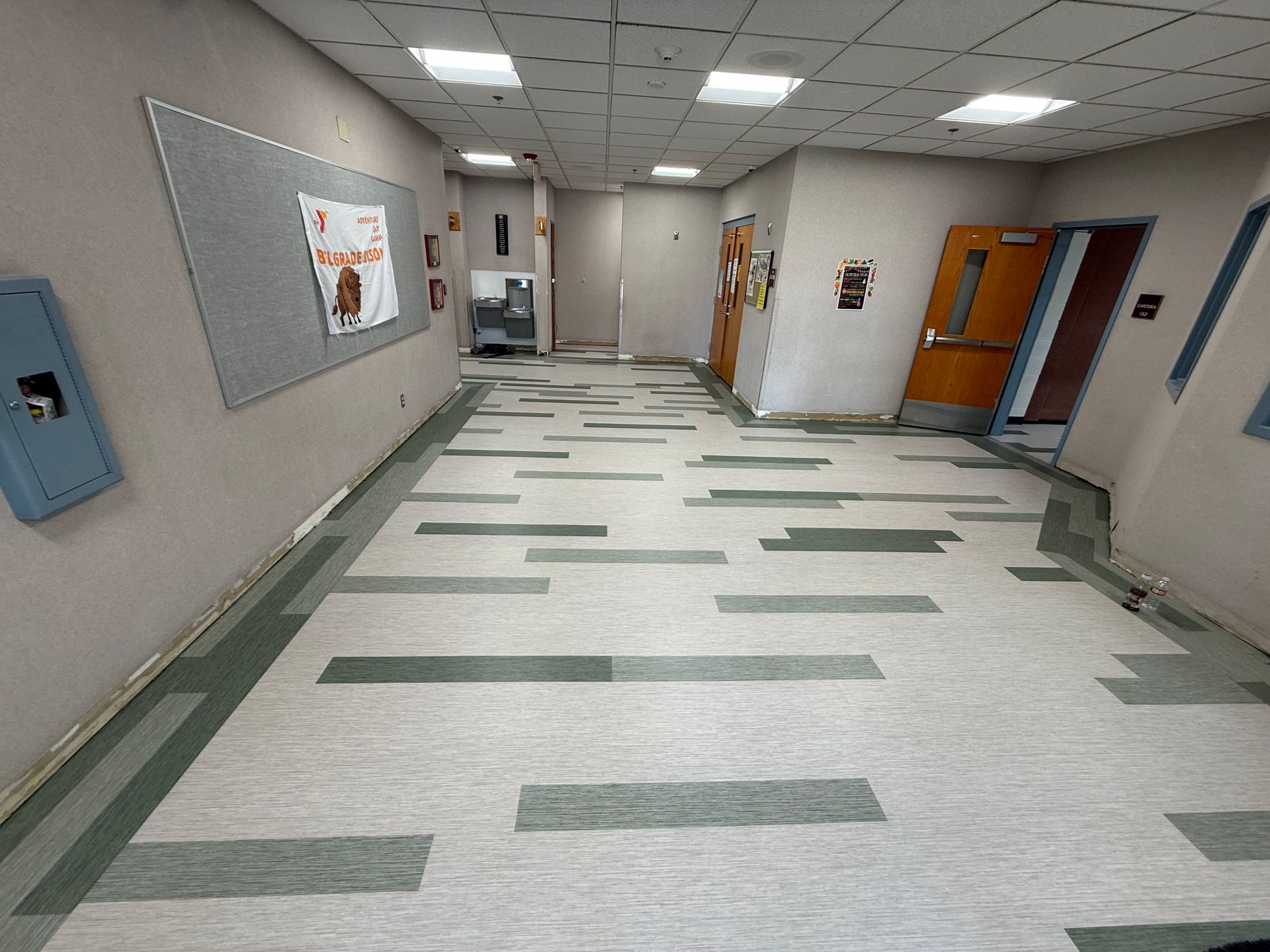 Empty school hallway with white walls, green-tile floor, and classroom doors on the right.
