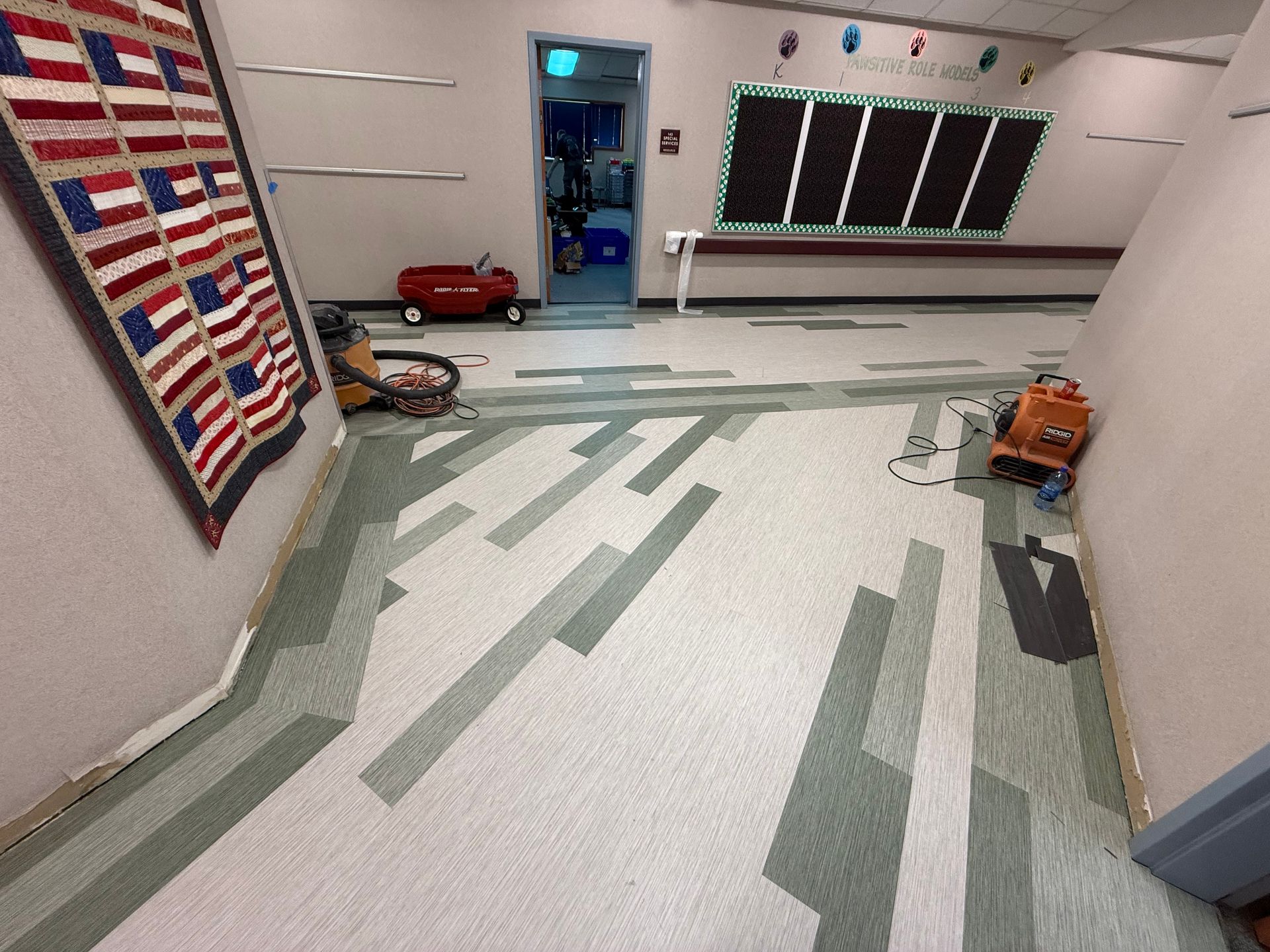 Empty garage workshop with white floor, green stripes, wall quilt, tools, and an open doorway.