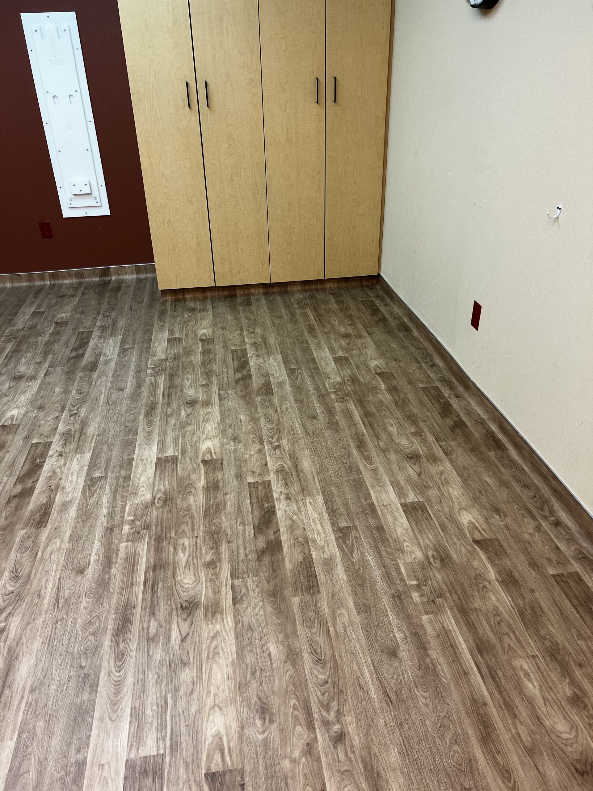 Empty room with wood flooring, beige walls, and a built-in closet near a red door.