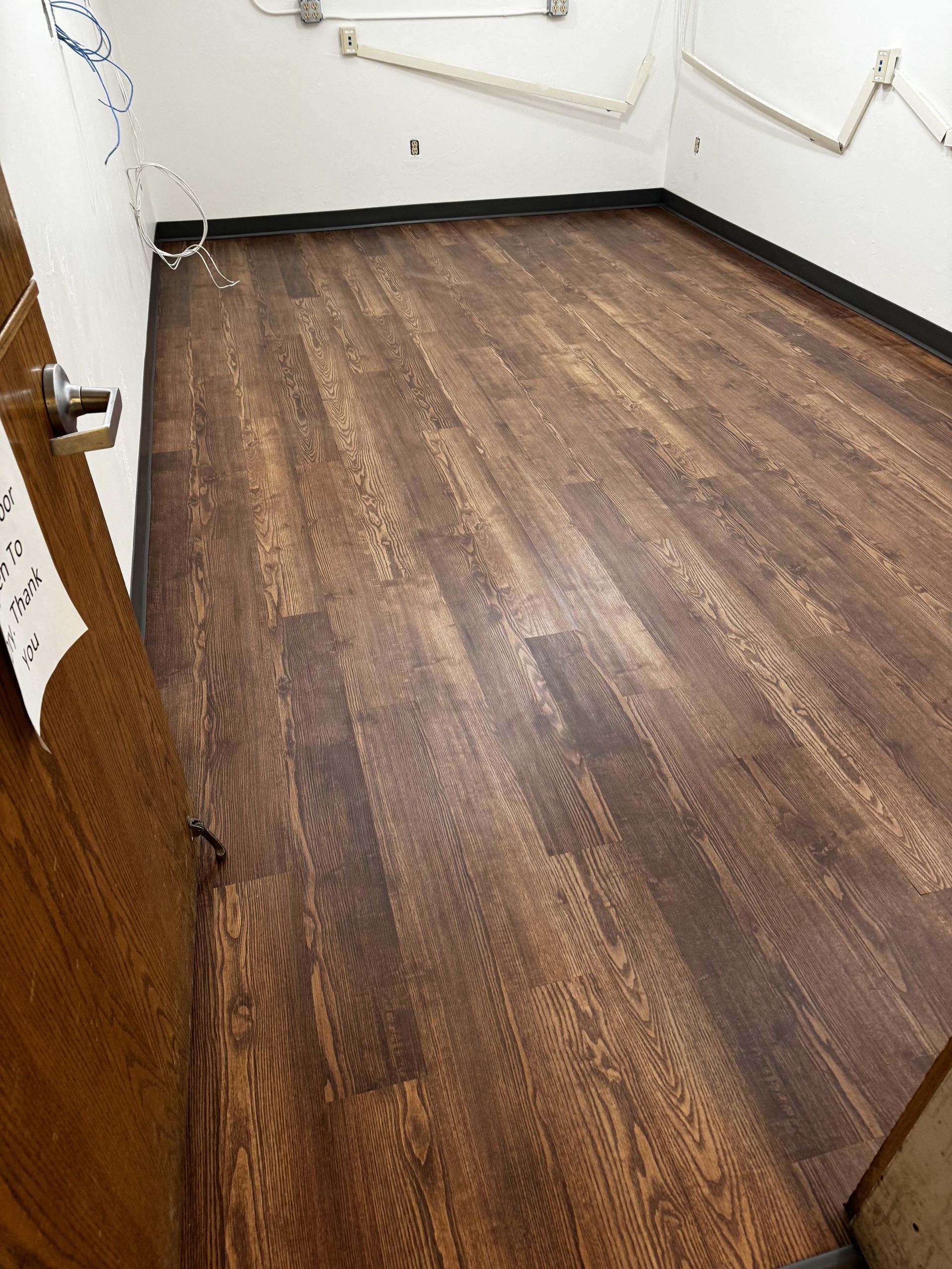 Empty room with dark wood flooring and white walls, viewed from an open doorway.