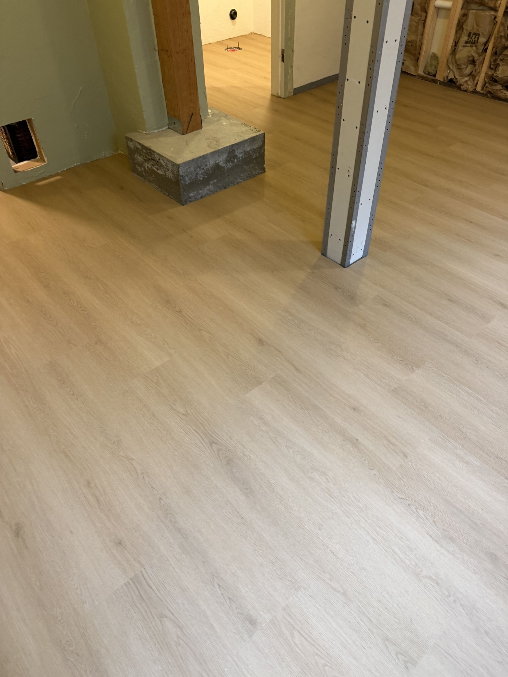 Empty room with light wood flooring, an open doorway, and a small gray block near the wall.