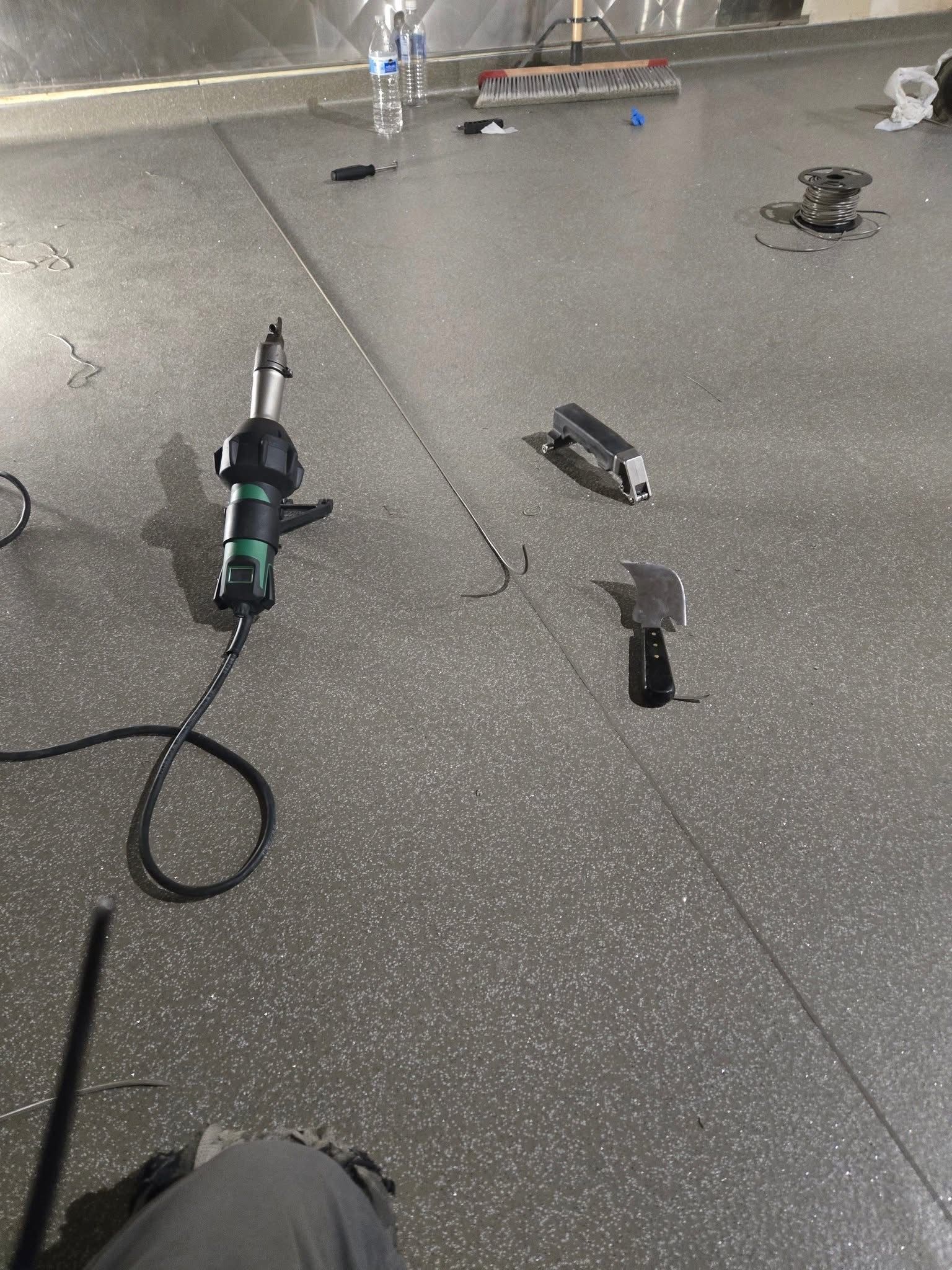 Spilled black power tool parts scattered on a speckled concrete floor in a workshop or garage.