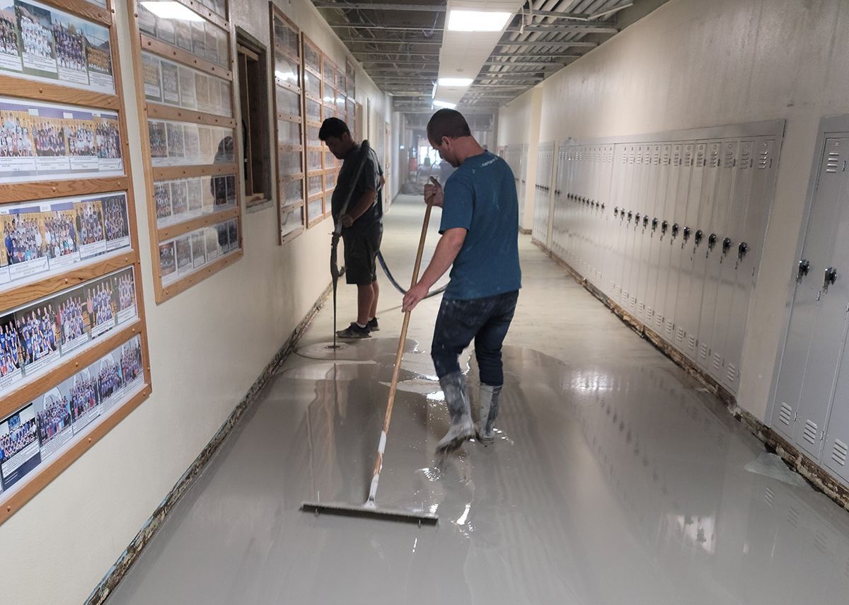 Two workers cleaning a hallway floor with mops and a floor squeegee in a bright corridor.