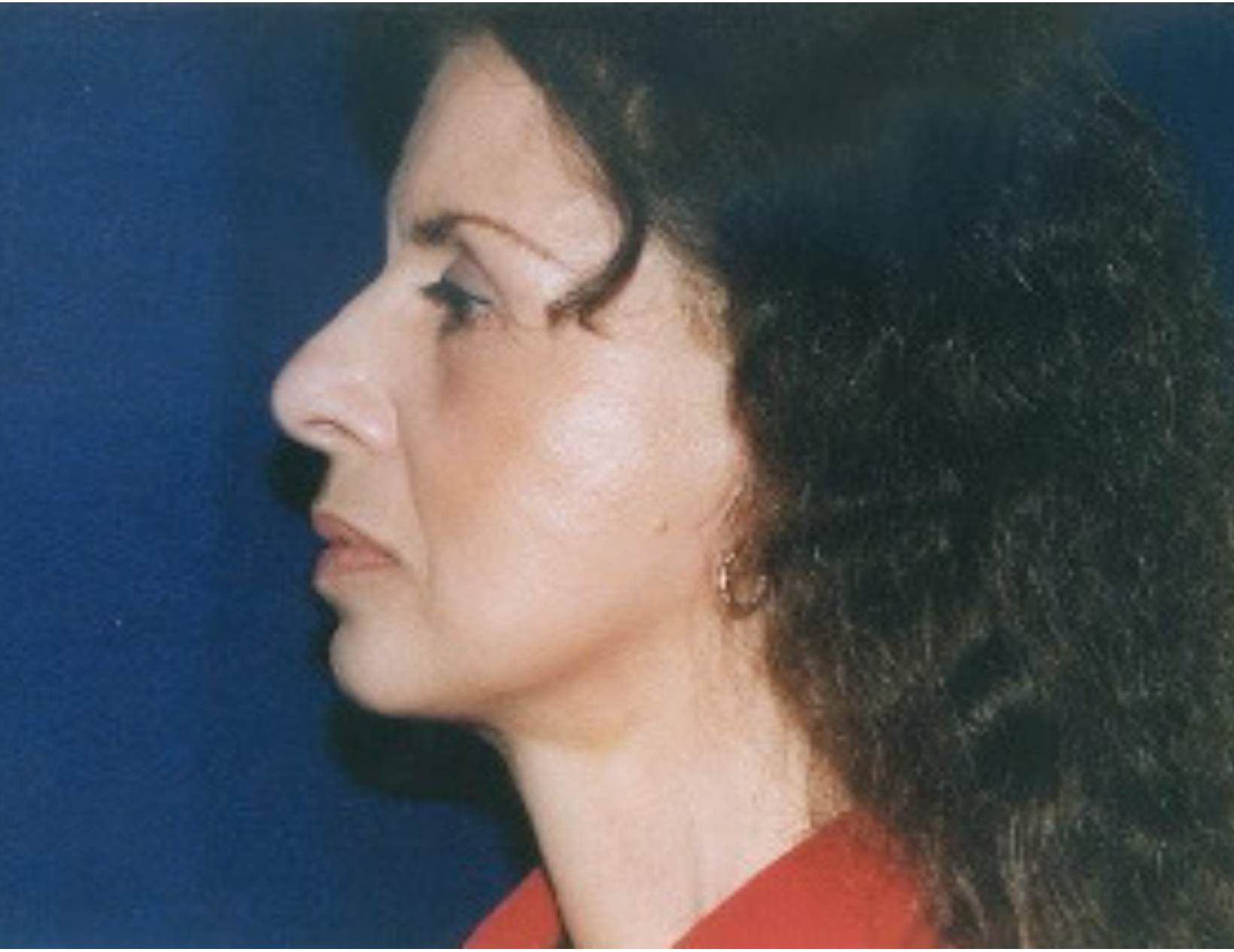 A woman with long hair is wearing a red shirt and earrings.