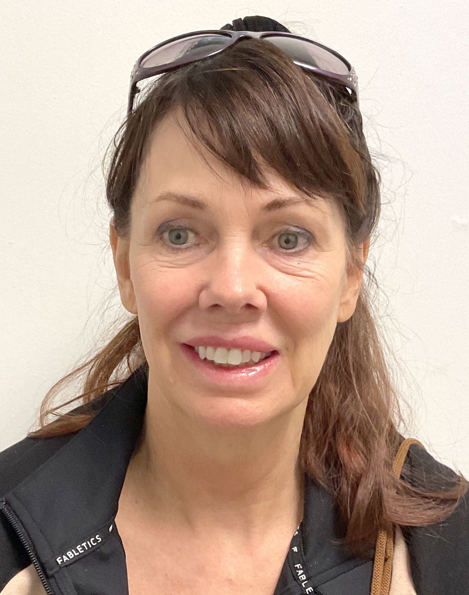 A woman wearing sunglasses and a jacket is smiling for the camera