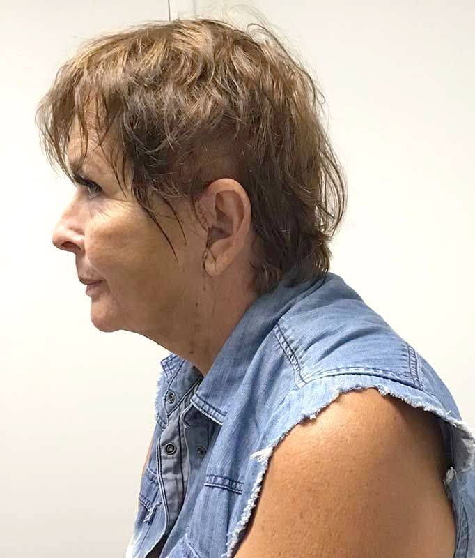 A woman in a denim vest is sitting in front of a white wall
