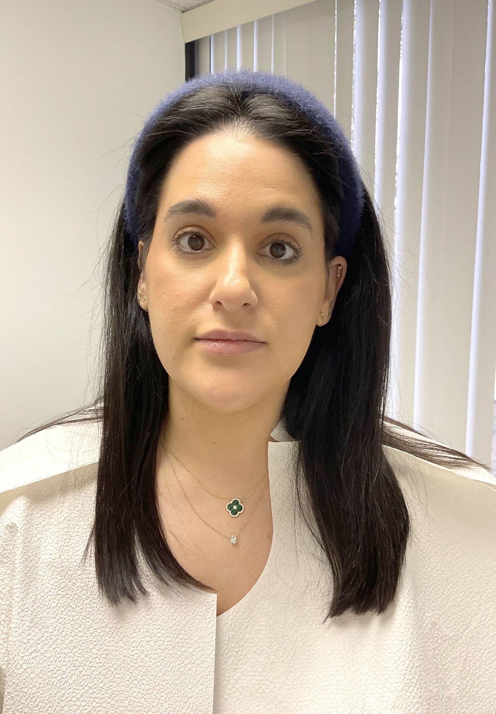 A woman wearing a headband and a white jacket is looking at the camera