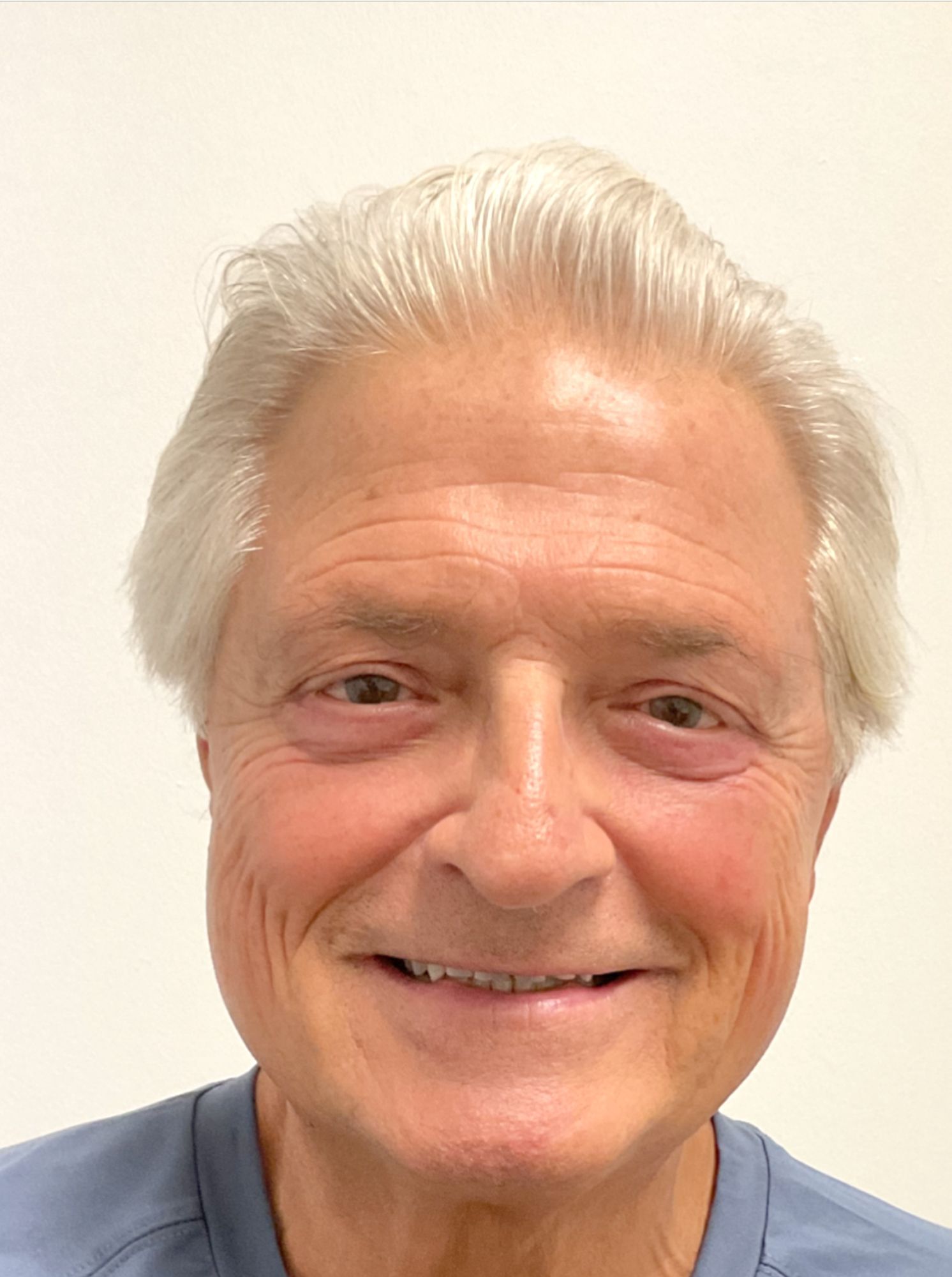 A man with white hair and a blue shirt is smiling for the camera