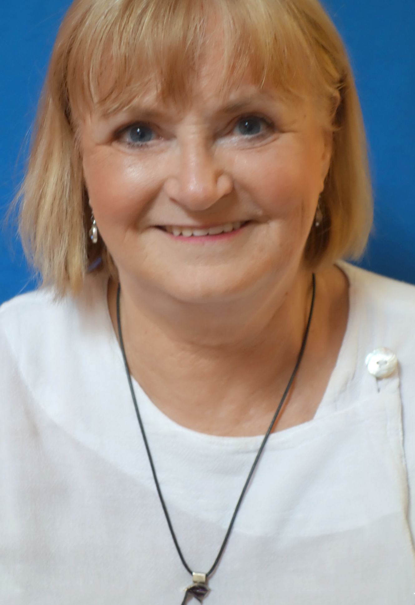 A woman wearing a white shirt and a black necklace is smiling
