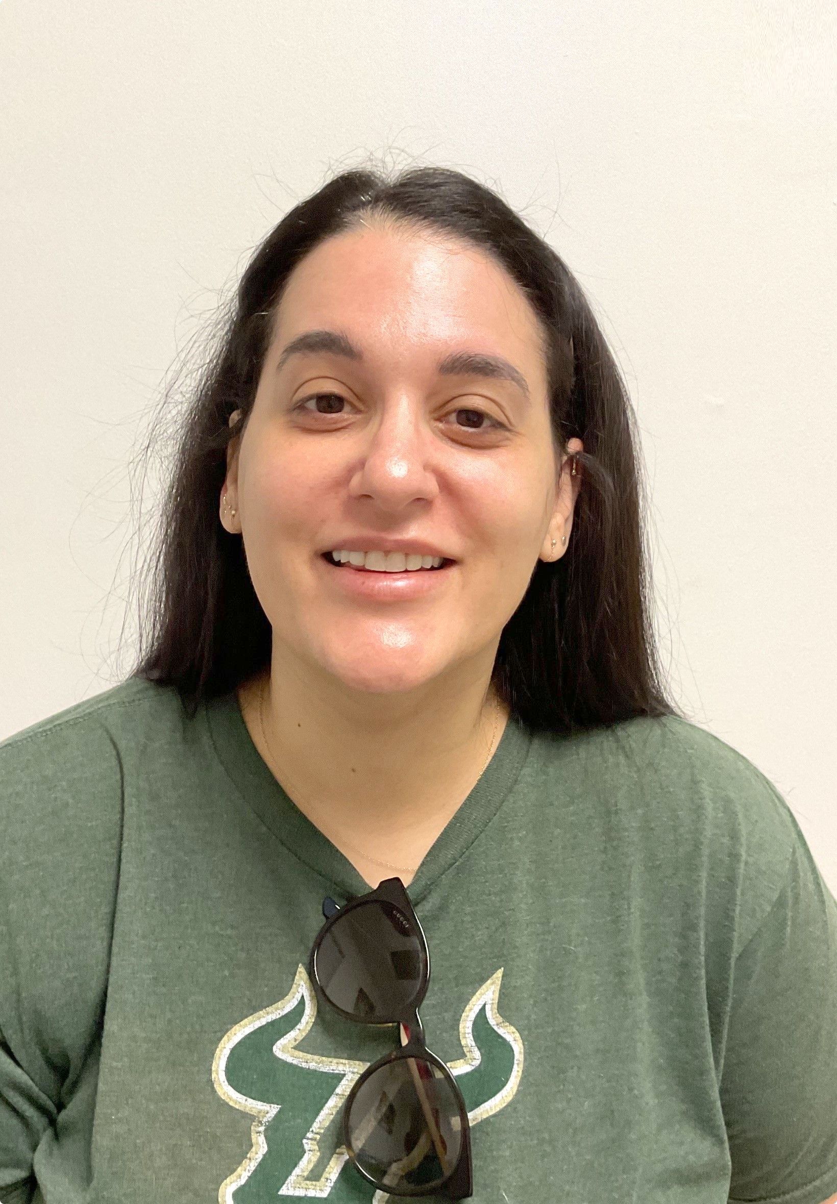 A woman wearing a green shirt and sunglasses is smiling for the camera
