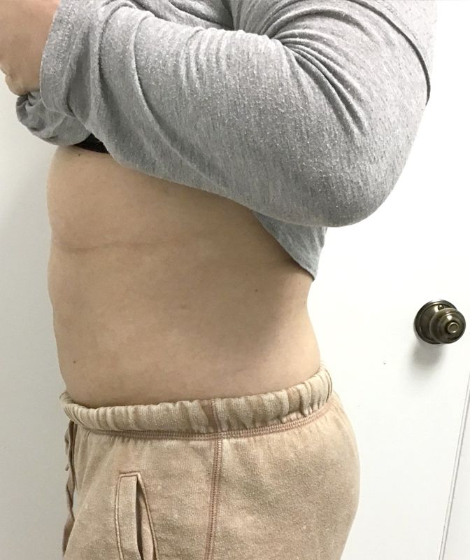 A woman is standing in front of a door wearing shorts and a gray shirt