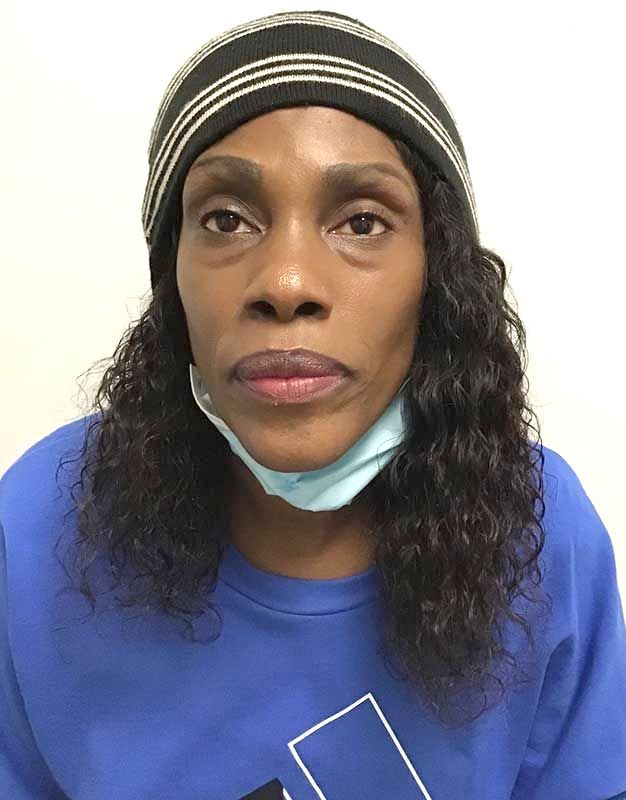 A woman wearing a mask and a beanie looks at the camera