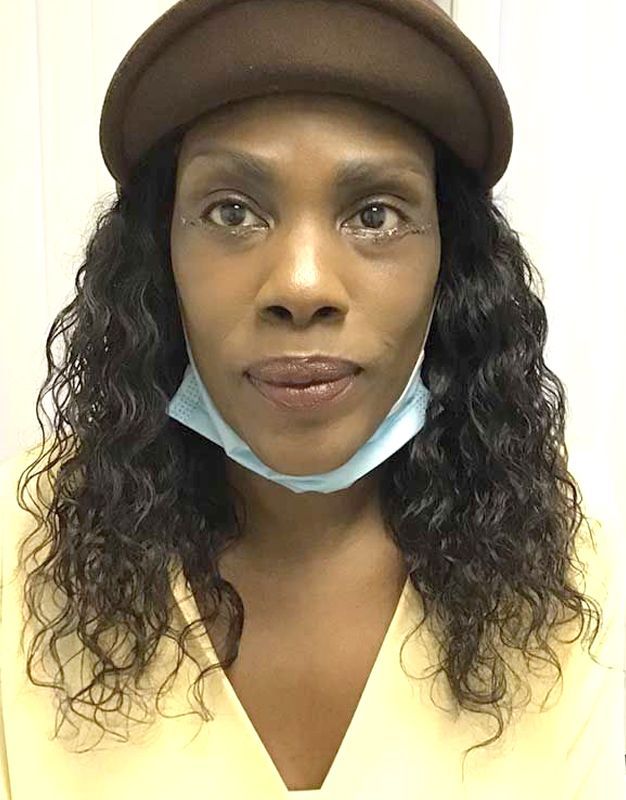 A woman wearing a hat and a mask looks at the camera