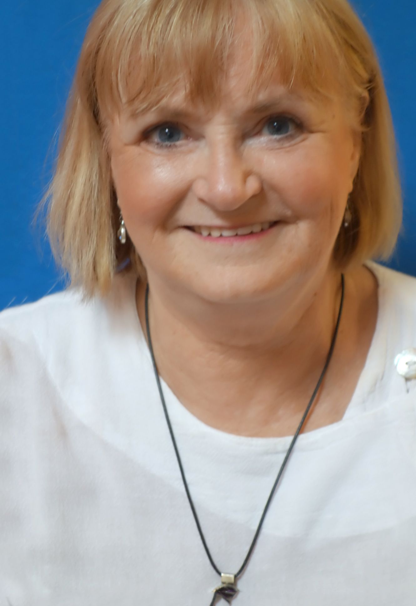 A woman wearing a white shirt and a black necklace is smiling