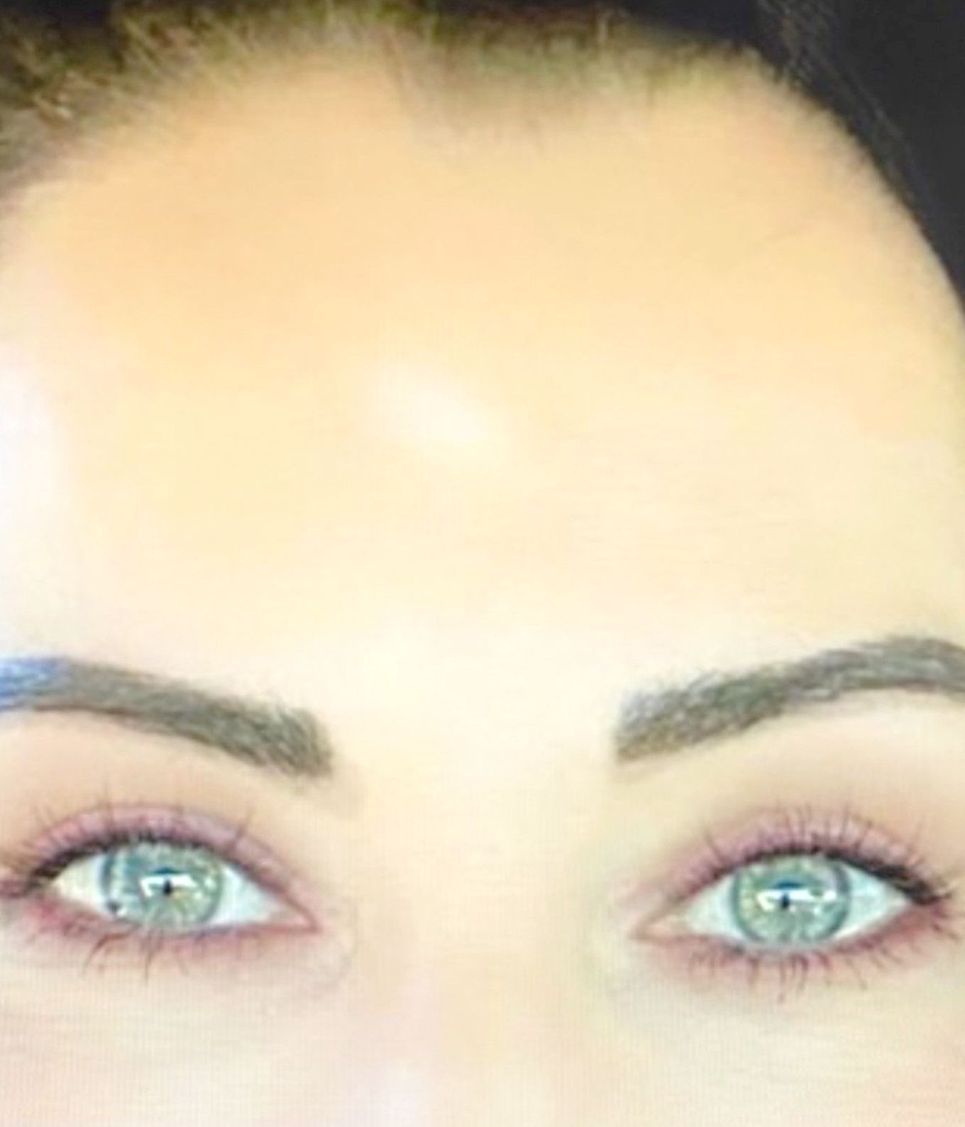 A close up of a woman's face with green eyes and brown eyebrows