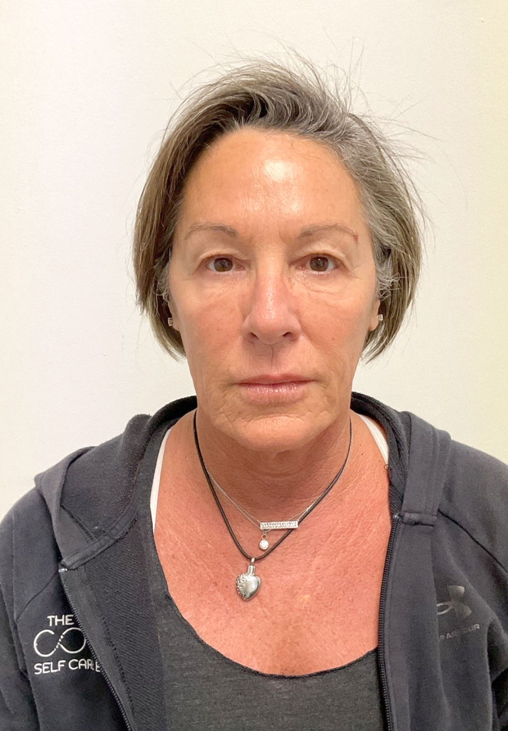 A woman wearing a gym shirt and a necklace is standing in front of a white wall