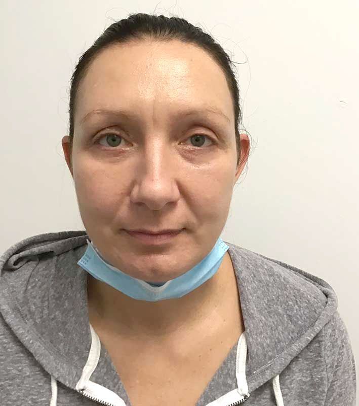 A woman wearing a gray hoodie and a blue mask around her neck