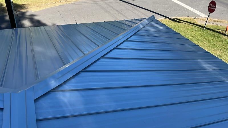 A blue metal roof is sitting on top of a house next to a road.