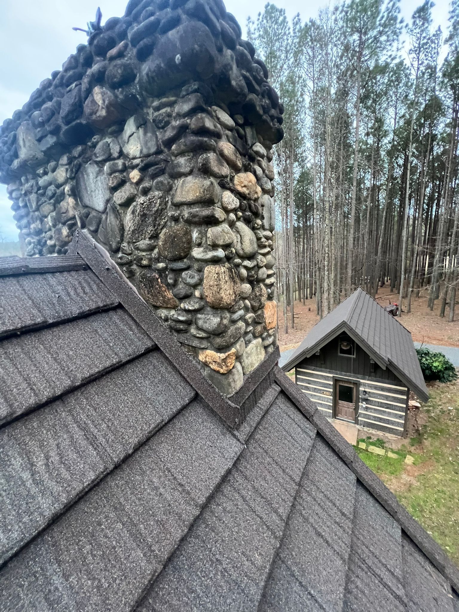 A stone chimney on top of a roof next to a cabin in the woods.