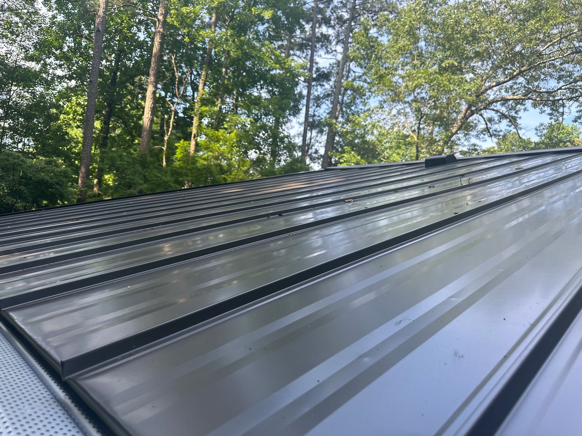 A close up of a metal roof with trees in the background