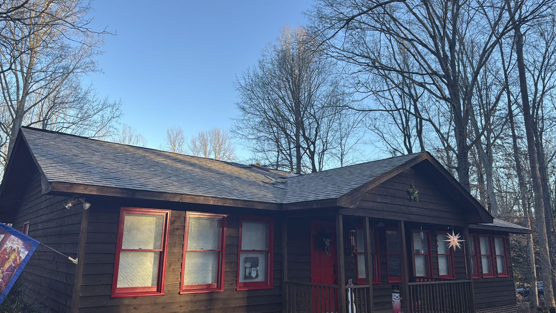 A wooden house with a red door and red windows is surrounded by trees on a sunny day.