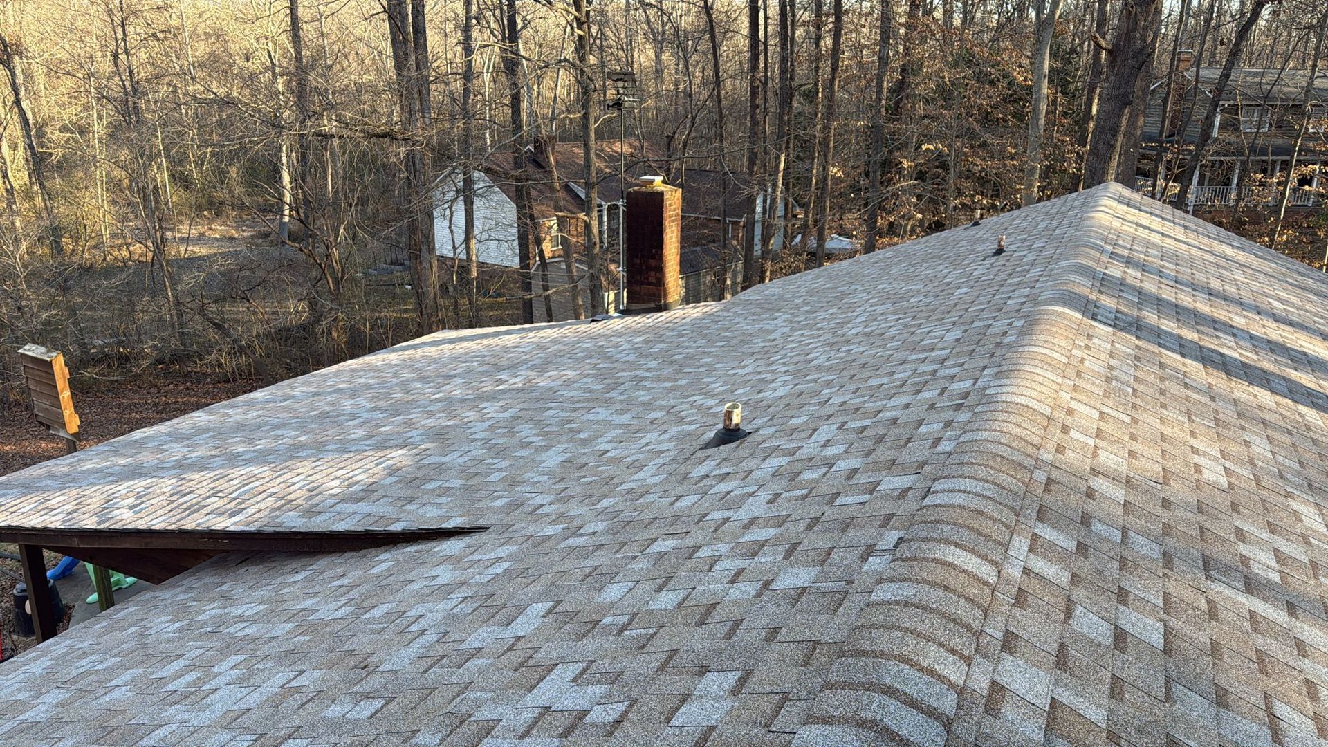 A close up of a roof with a chimney and trees in the background.