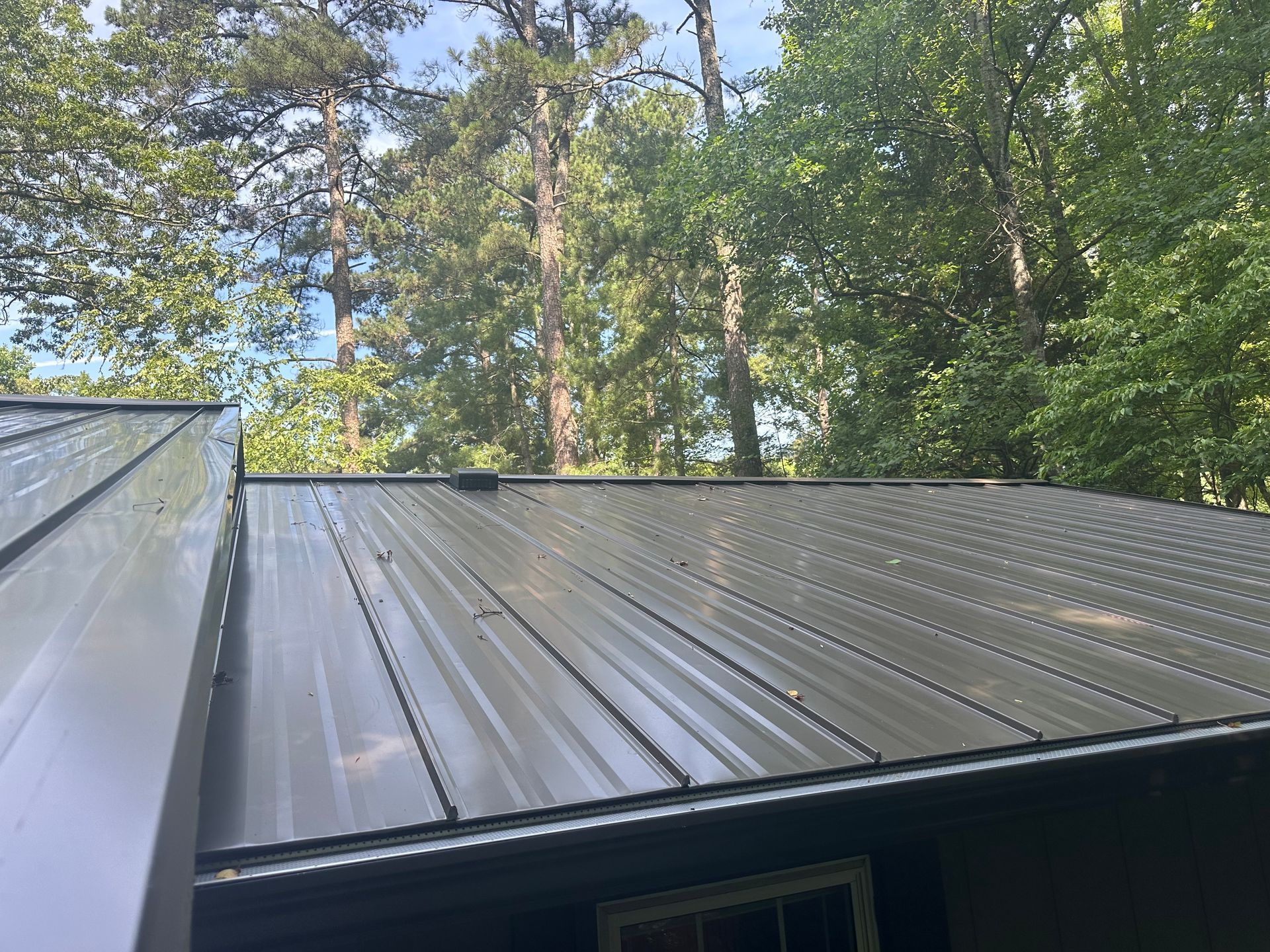 A metal roof on a house with trees in the background.