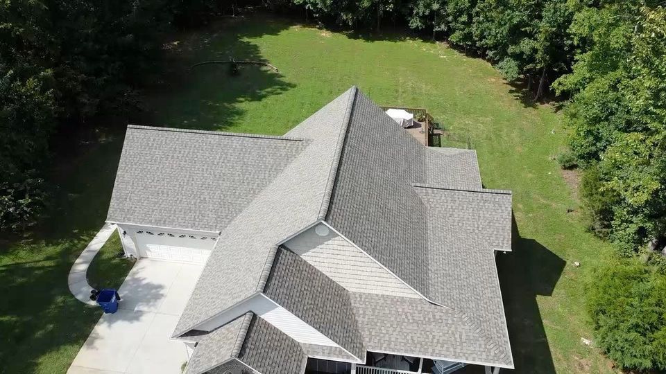 An aerial view of a large house with a gray roof surrounded by trees.