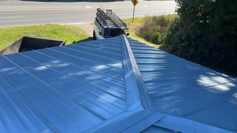 A metal roof is being installed on a house next to a road.