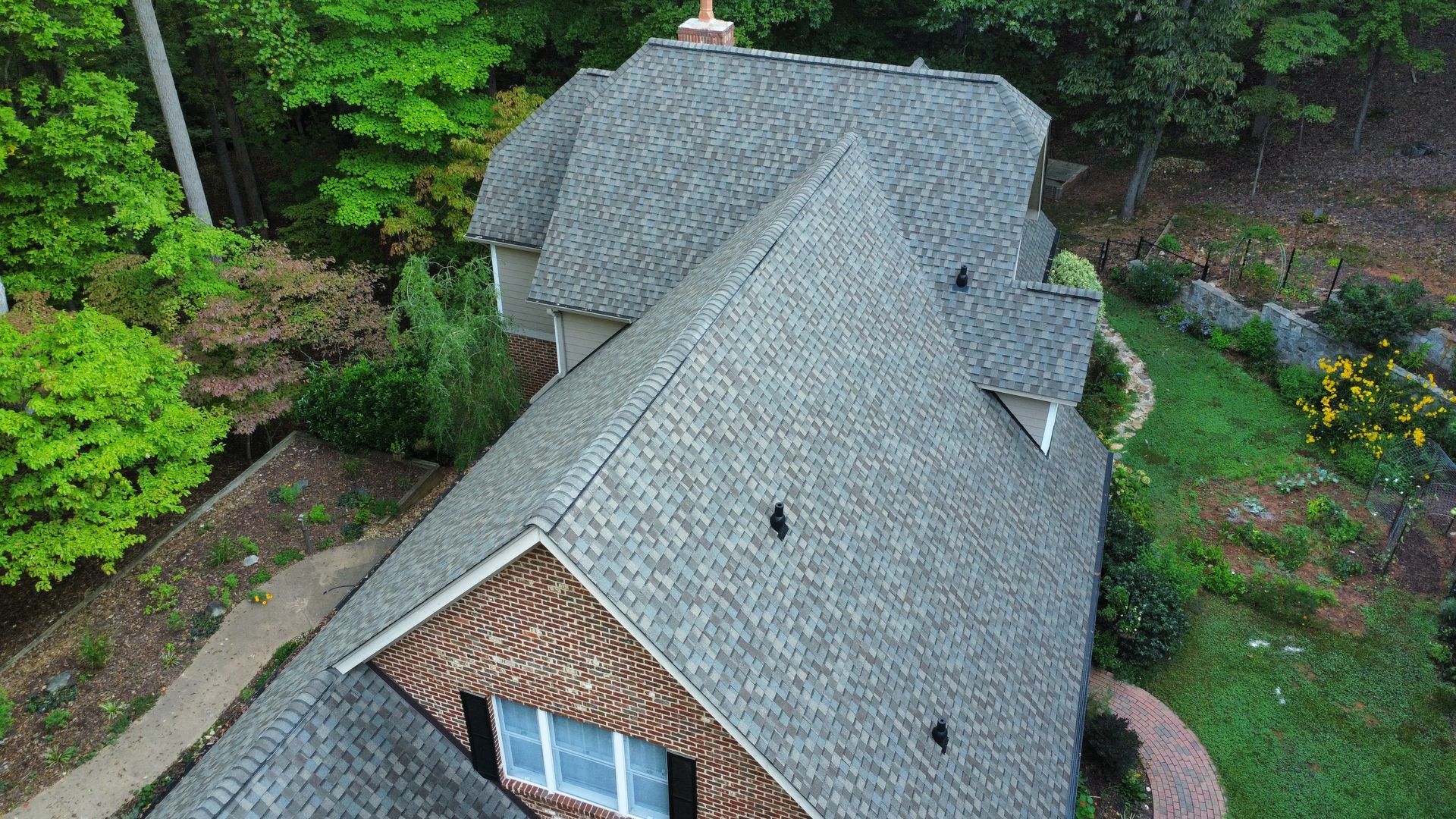 An aerial view of a brick house with a gray roof surrounded by trees.