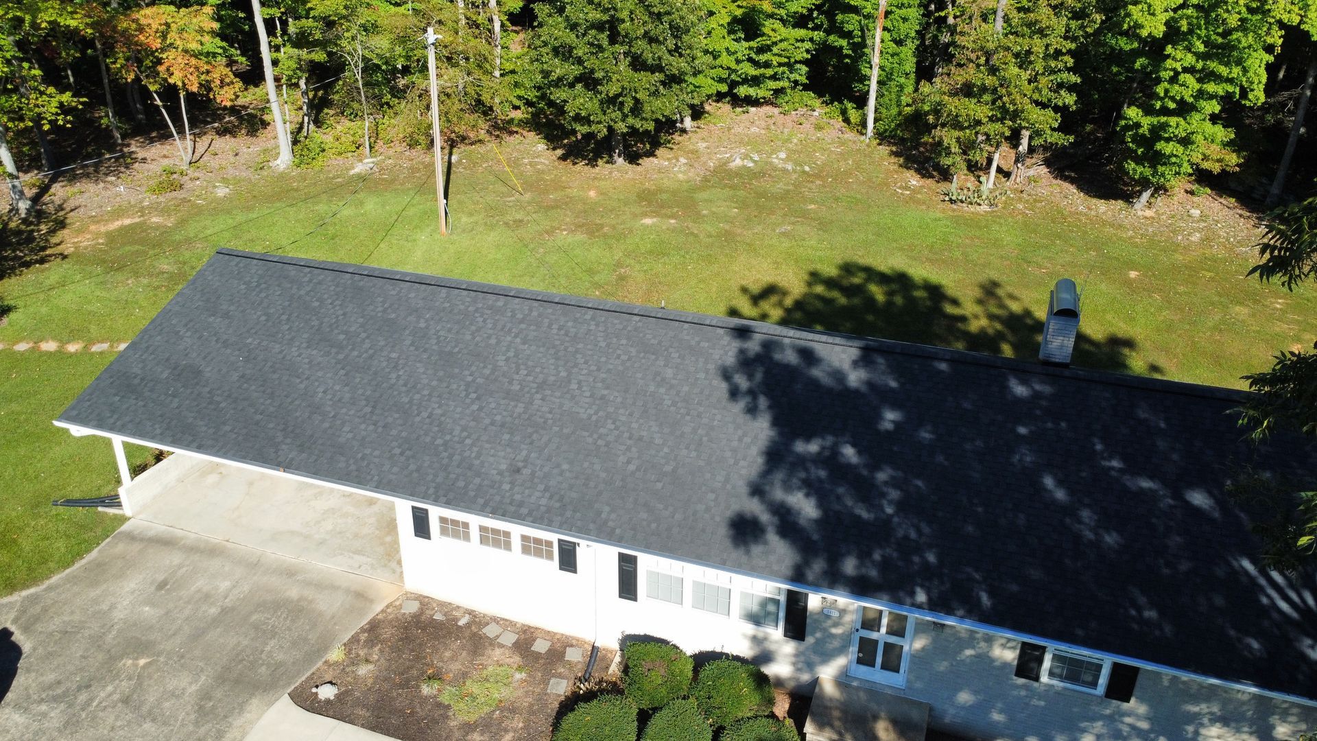 An aerial view of a house with a black roof surrounded by trees.