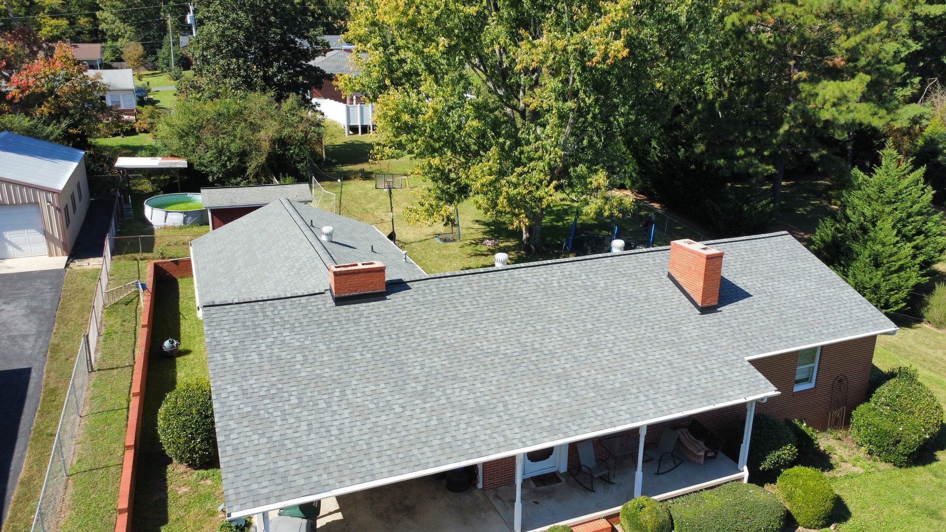 An aerial view of a house with a roof and a porch surrounded by trees.