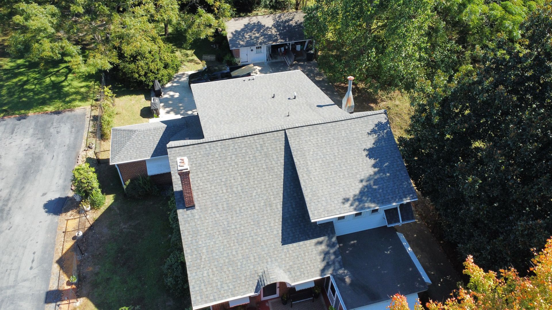 An aerial view of a house with a roof that is surrounded by trees.
